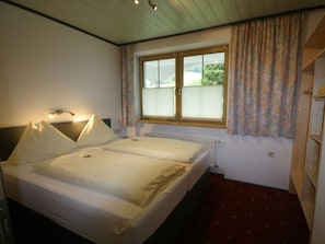 Een kamer met twee bedden, een raam met zonwering, een radiator en een houten plafond.