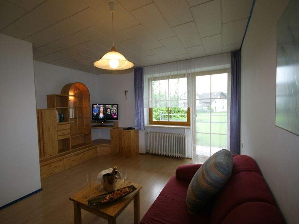 A living room with a wooden cabinet, a television, a red sofa, and a window with a view of greenery.
