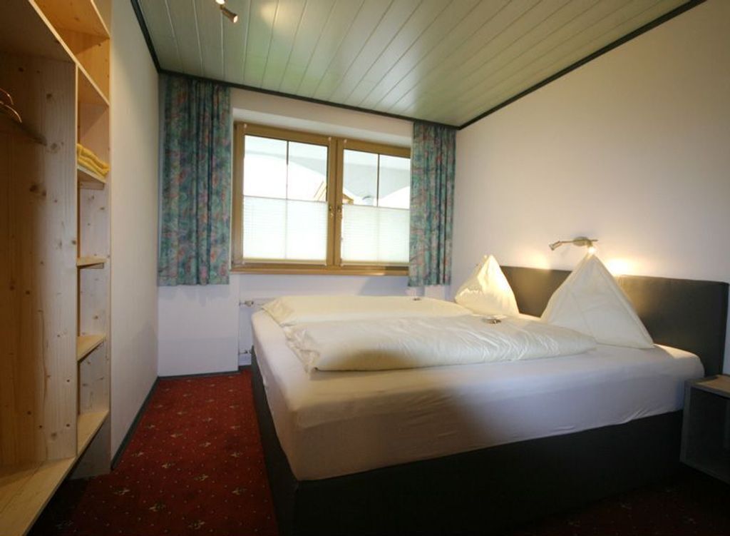 Un dormitorio con cama, mesita de noche, ventana con cortinas y armario.
