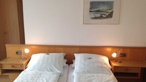 Un lit double avec du linge de lit blanc, deux tables de chevet avec des lampes, une tête de lit en bois et un tableau encadré au mur.