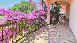 A balcony with a tiled floor and a metal railing, surrounded by pink flowers and greenery. - Holiday apartment with air conditioning and barbecue (Medulin)