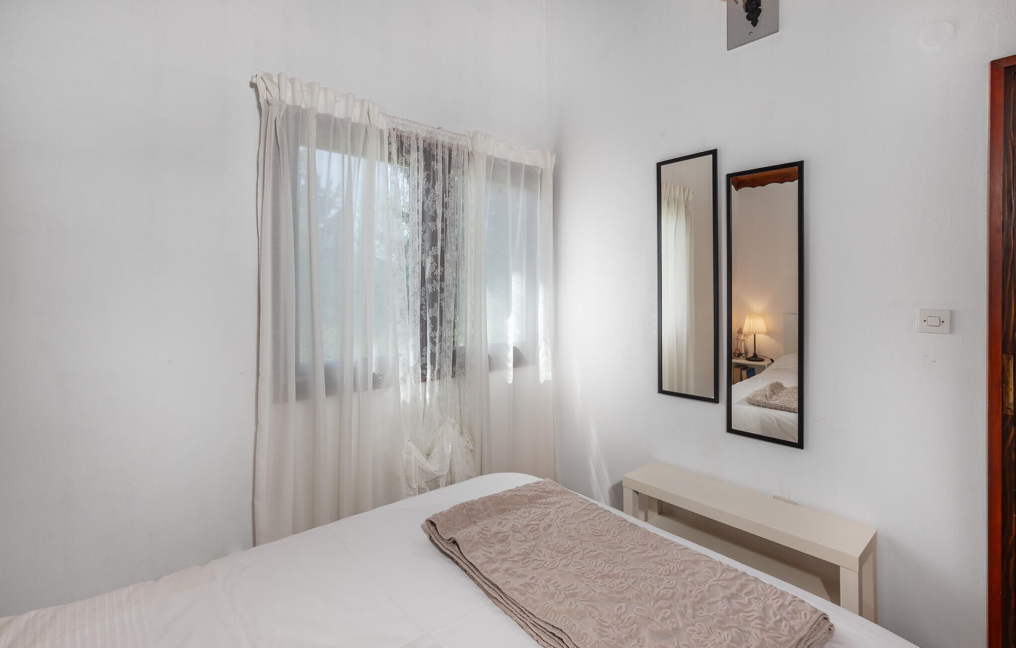 Een slaapkamer met een bed, een nachtkastje, een lamp en twee spiegelbeeldige lijsten aan de muur.