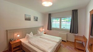 Ein Schlafzimmer mit Bett, Nachttischen, einem Heizgerät, einem Fenster mit Vorhängen und Wandbildern.