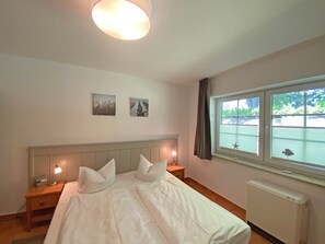 Ein Schlafzimmer mit einem großen Bett, zwei Nachttischen, einem Fenster mit Blick auf ein Gewässer und zwei an der Wand befestigten Bildern.
