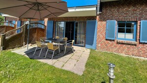 Eine Terrasse mit Tisch und Stühlen, einem großen Sonnenschirm und einer Holztreppe zu einer Außenterrasse.