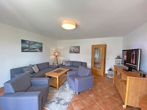 Ein Wohnzimmer mit einem Ecksofa, einem Holztisch, einer Lampe, einem Fernseher und Kunstwerken an den Wänden.
