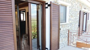 A room with a sliding glass door leading to a balcony, a stone wall, and a window with shutters.