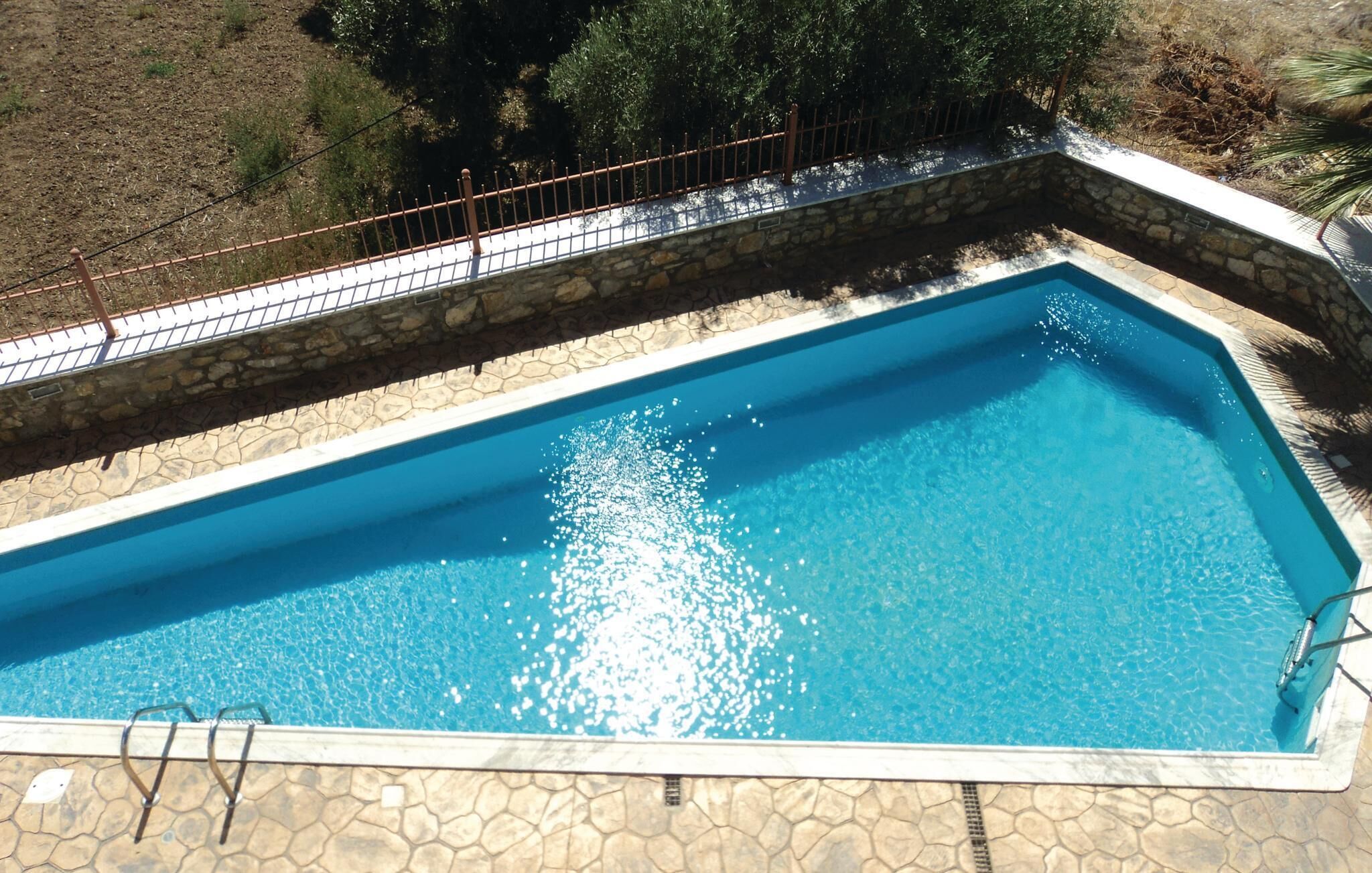 A rectangular swimming pool with a stone border and a metal fence.