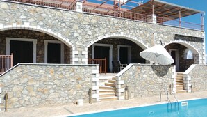 A stone building with a pool, featuring arched doorways and a staircase leading to a balcony.