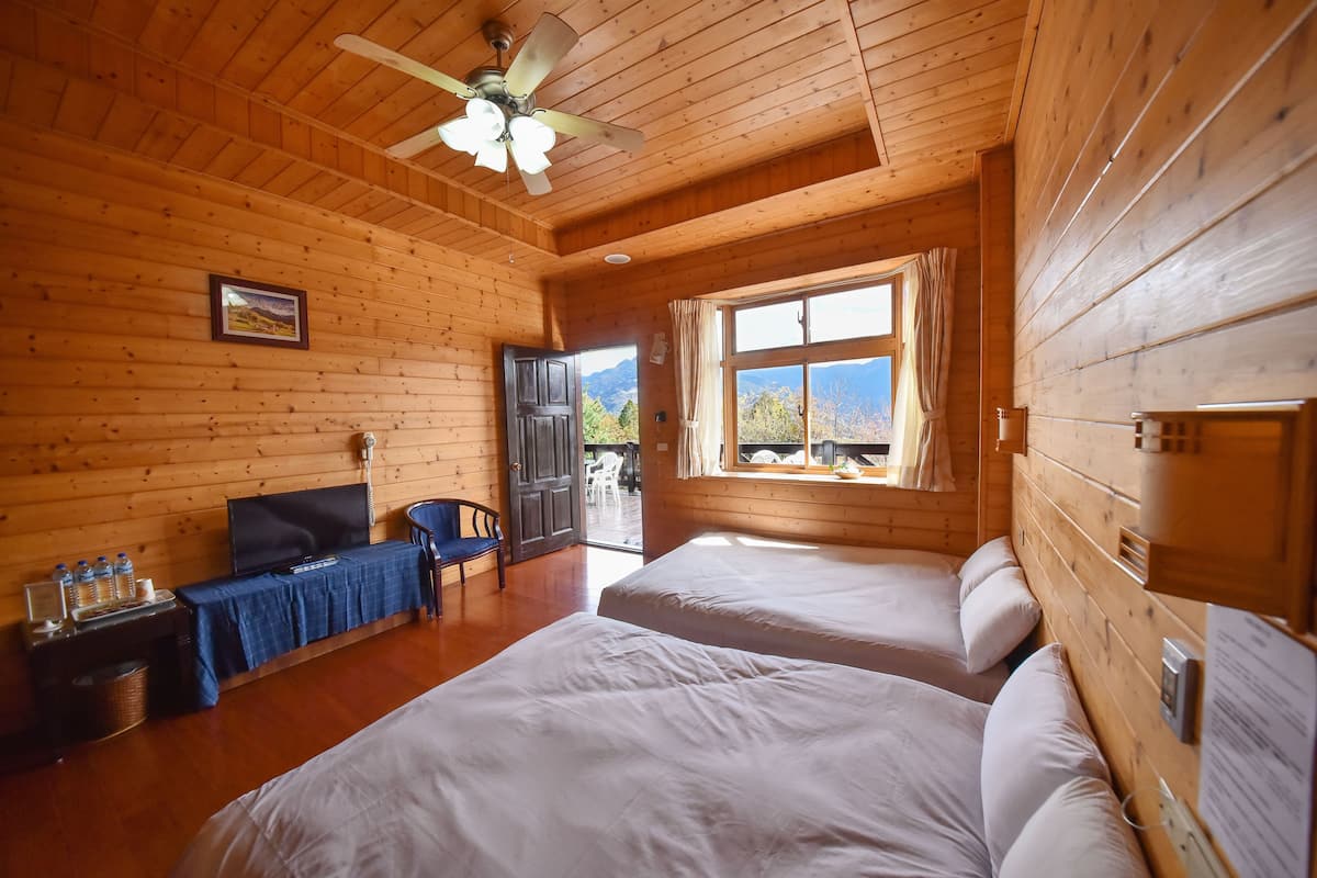 Habitación de cabaña de madera con dos camas, un televisor, un escritorio con silla y una ventana con vista a la montaña.