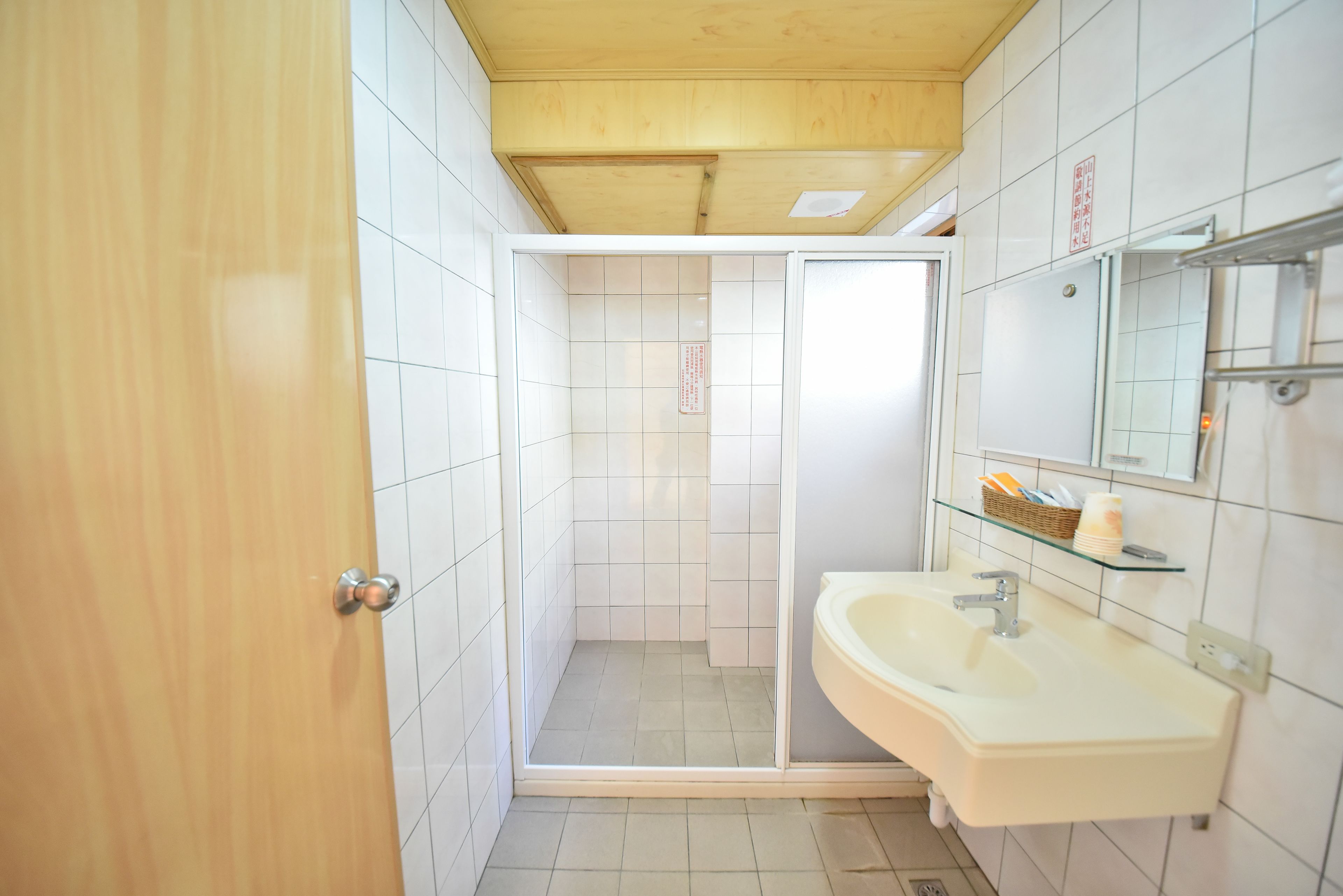A bathroom with a wooden door, a shower, and a sink with a mirror.