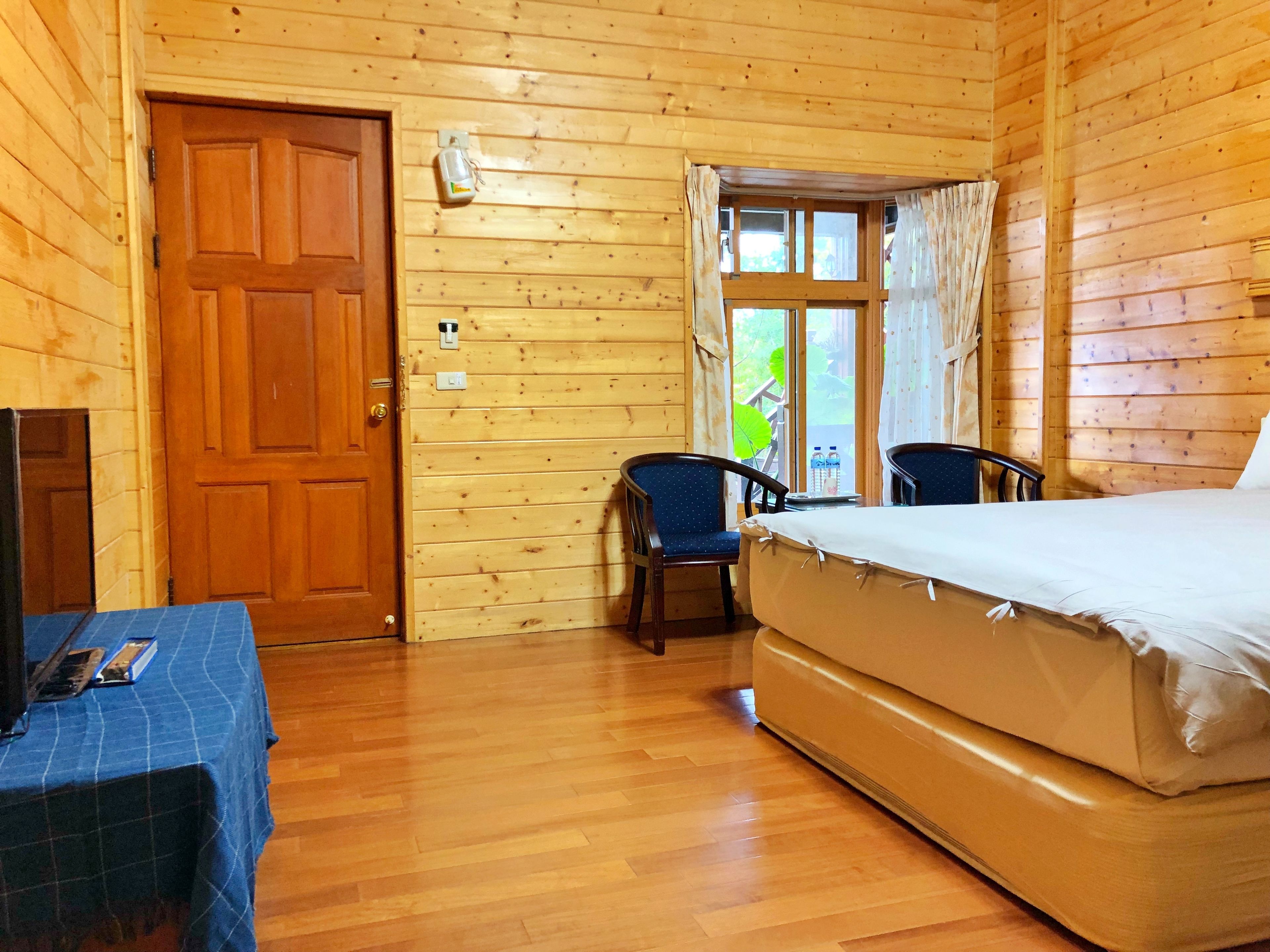 A wooden cabin room with a bed, two chairs, a table, and a door.