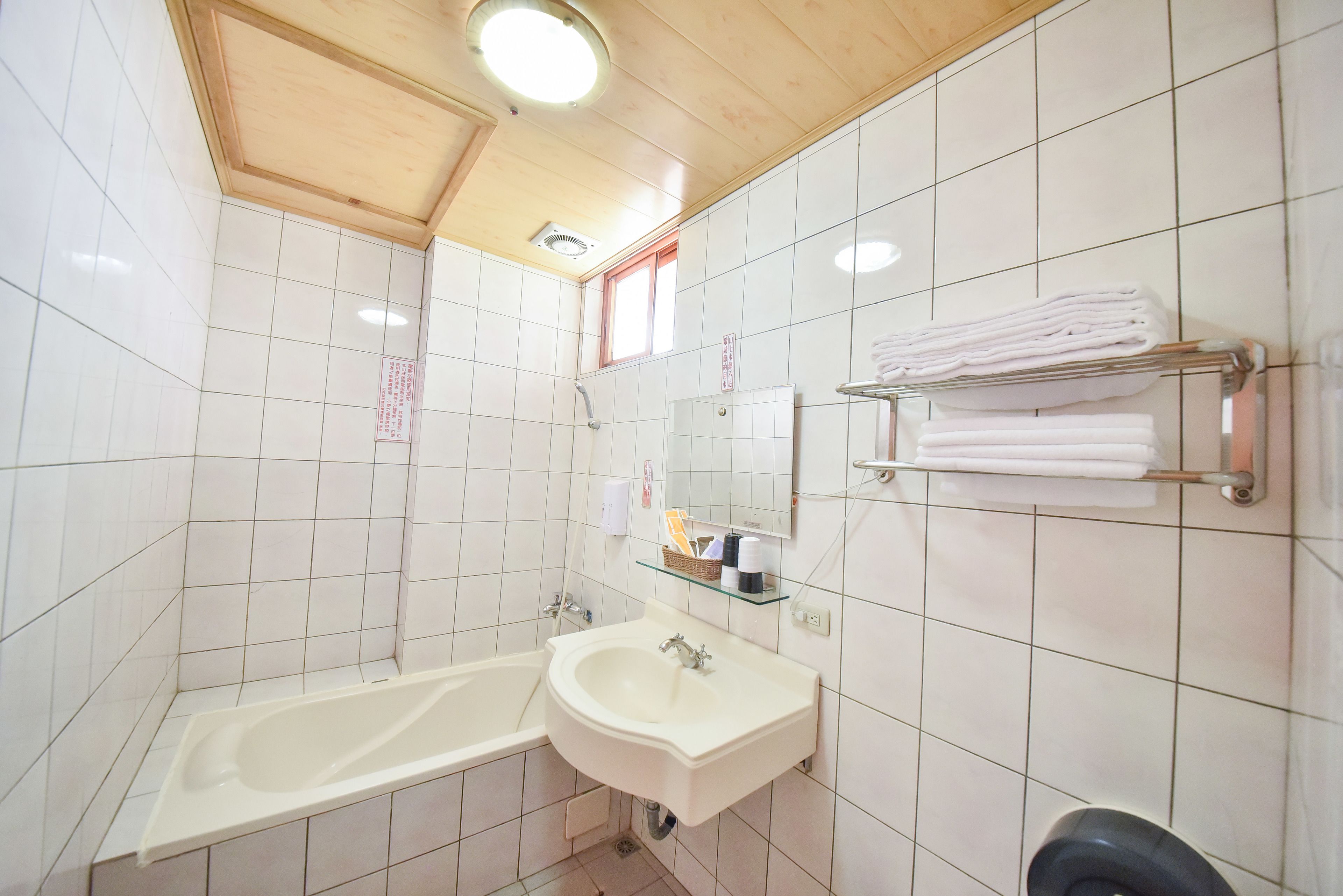 A bathroom with white tiled walls, a wooden ceiling, a bathtub, a sink, and a towel rack.