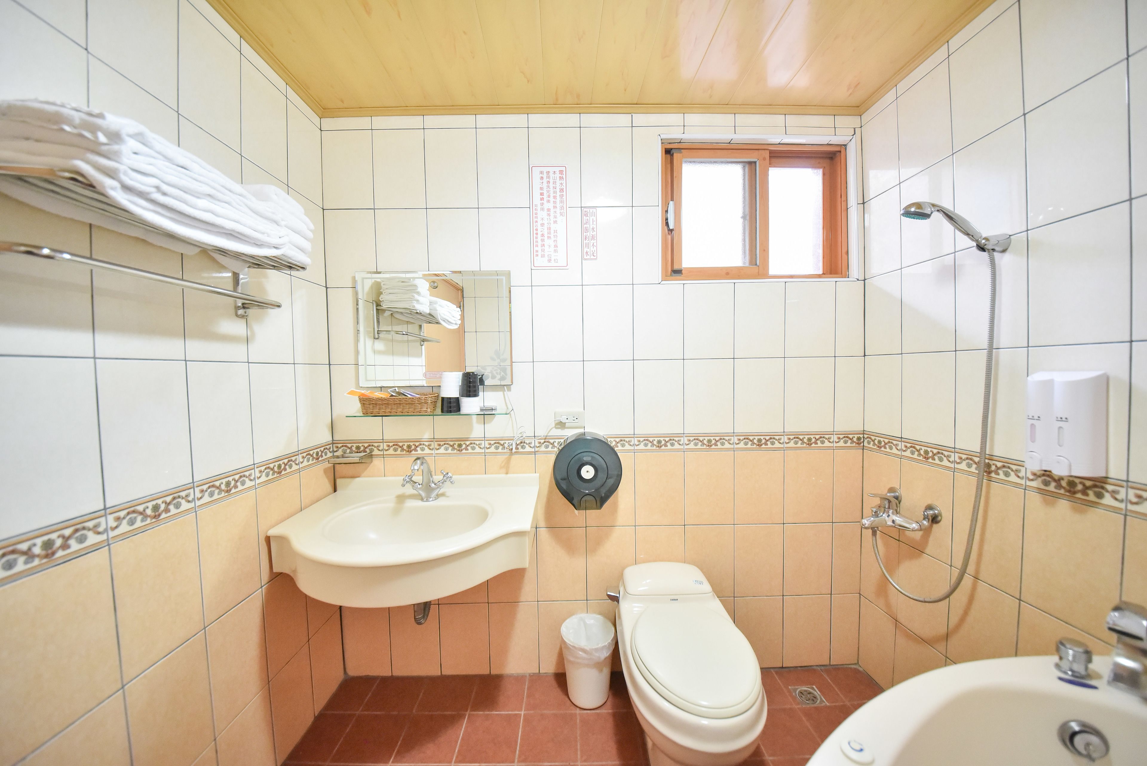 Un baño con lavamanos, inodoro y ducha. Hay un perchero y una ventana.