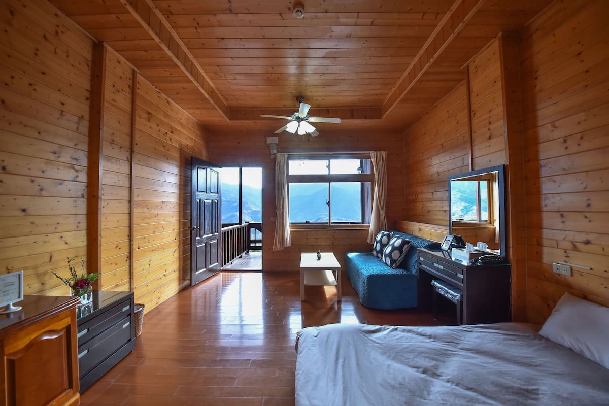 Habitación de cabaña de madera con cama, sofá, escritorio y ventanas amplias que ofrecen vistas.