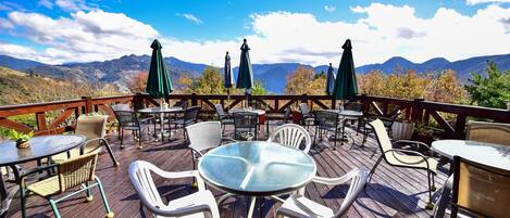 A wooden deck with outdoor seating, including round tables and chairs, and umbrellas providing shade.