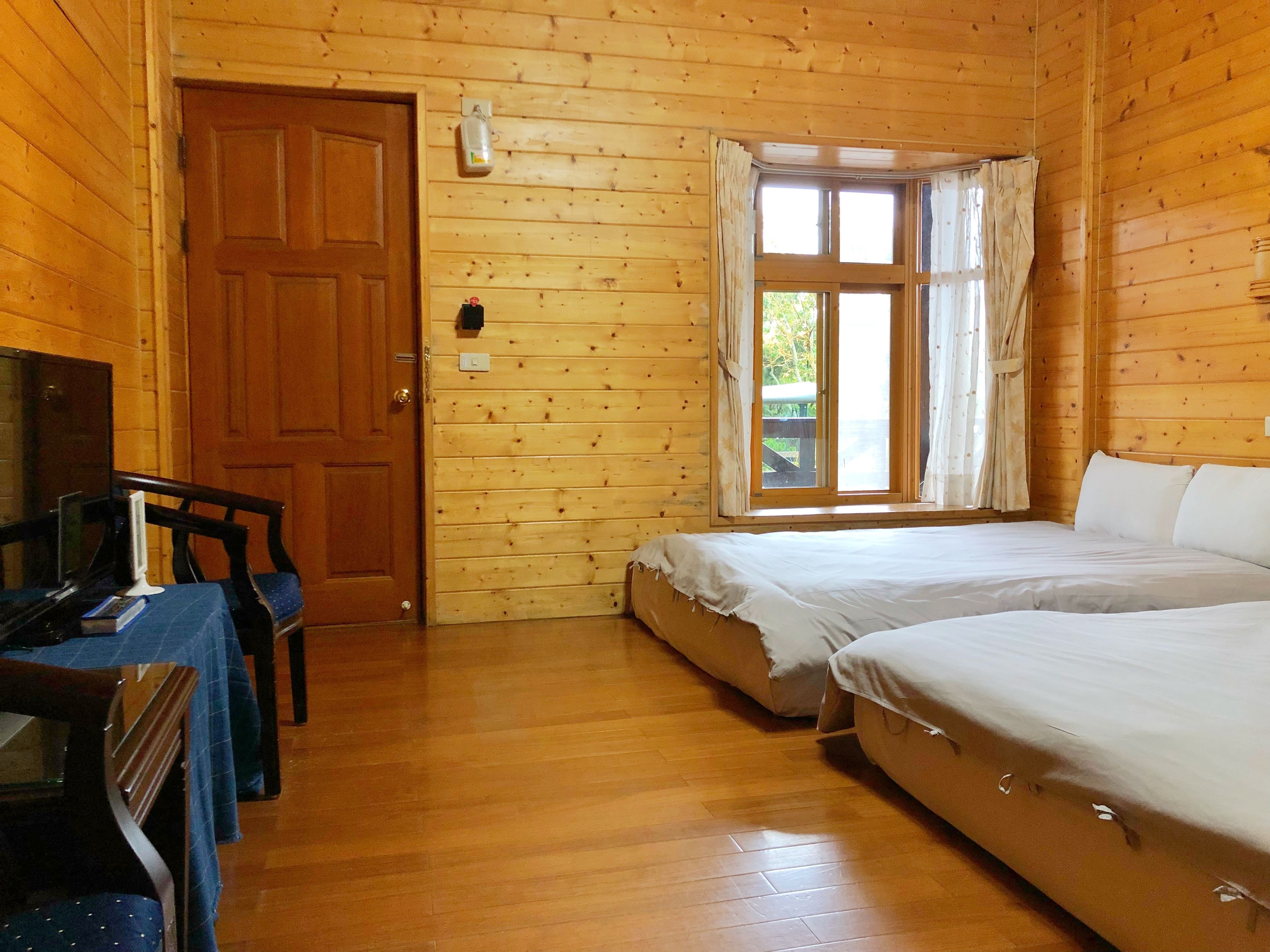Ein Zimmer in einer Holzhütte mit zwei Betten, einem Schreibtisch mit Computer und einem Fenster mit Vorhängen.