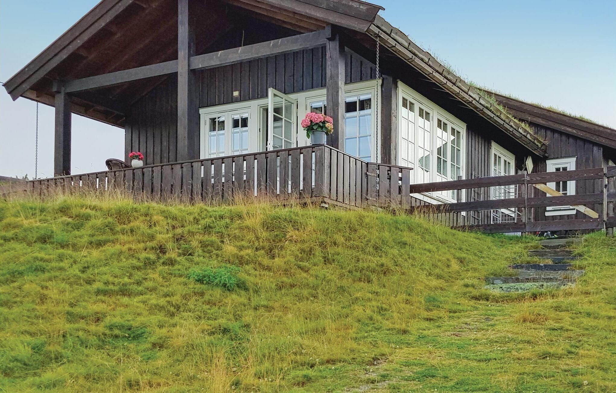 A rustic wooden cabin with a porch, large windows, and a small garden area with flowers.