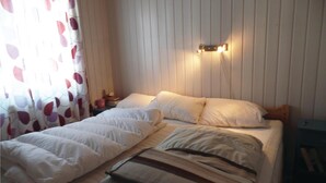 A bed with white bedding and a striped pillow, a nightstand with a lamp, and a curtain with a leaf pattern. - Amazing home in Kvam with kitchen (Kvam)