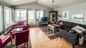 A cozy living room with a red sofa, a dark sofa, a wooden coffee table, and a TV. There are large windows with curtains, a wooden cabinet, and a fireplace. - Amazing home in Kvam with kitchen (Kvam)