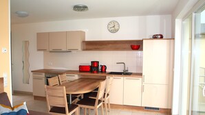 A modern kitchen with wooden cabinets, a dining table with chairs, a red coffee maker, and a clock on the wall.