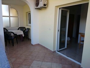 Uma área de refeições com mesa e cadeiras, uma porta de vidro deslizante que dá para uma varanda e um aparelho de ar condicionado na parede.