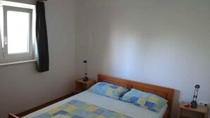 A single-bed room with a wooden headboard, a bedside table with a lamp, and a window with curtains. - Holiday apartment with air conditioning (Biograd na Moru)