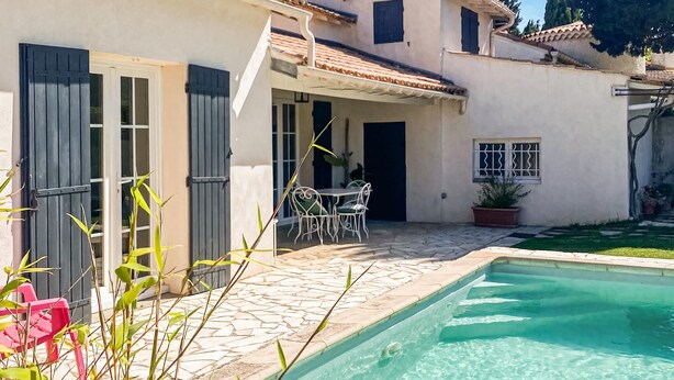 Un espace aménagé au bord de la piscine, avec une terrasse en pierre, une petite table et des chaises, ainsi qu’une plante en pot.