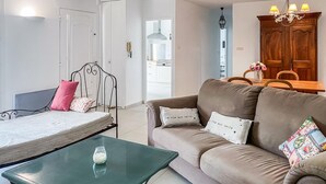 Un salon comprenant un lit, une table en verre vert, un canapé agrémenté de coussins décoratifs et un meuble en bois.