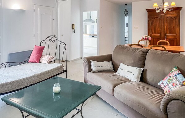 A living room with a bed, a green glass table, a sofa with decorative pillows, and a wooden cabinet.