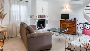 Un salon comprenant un canapé, une petite table, une cheminée, un téléviseur et un meuble.