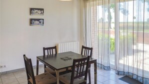 Un espace repas comprenant une table et des chaises, un luminaire suspendu et une vue sur l’extérieur à travers des rideaux légers.