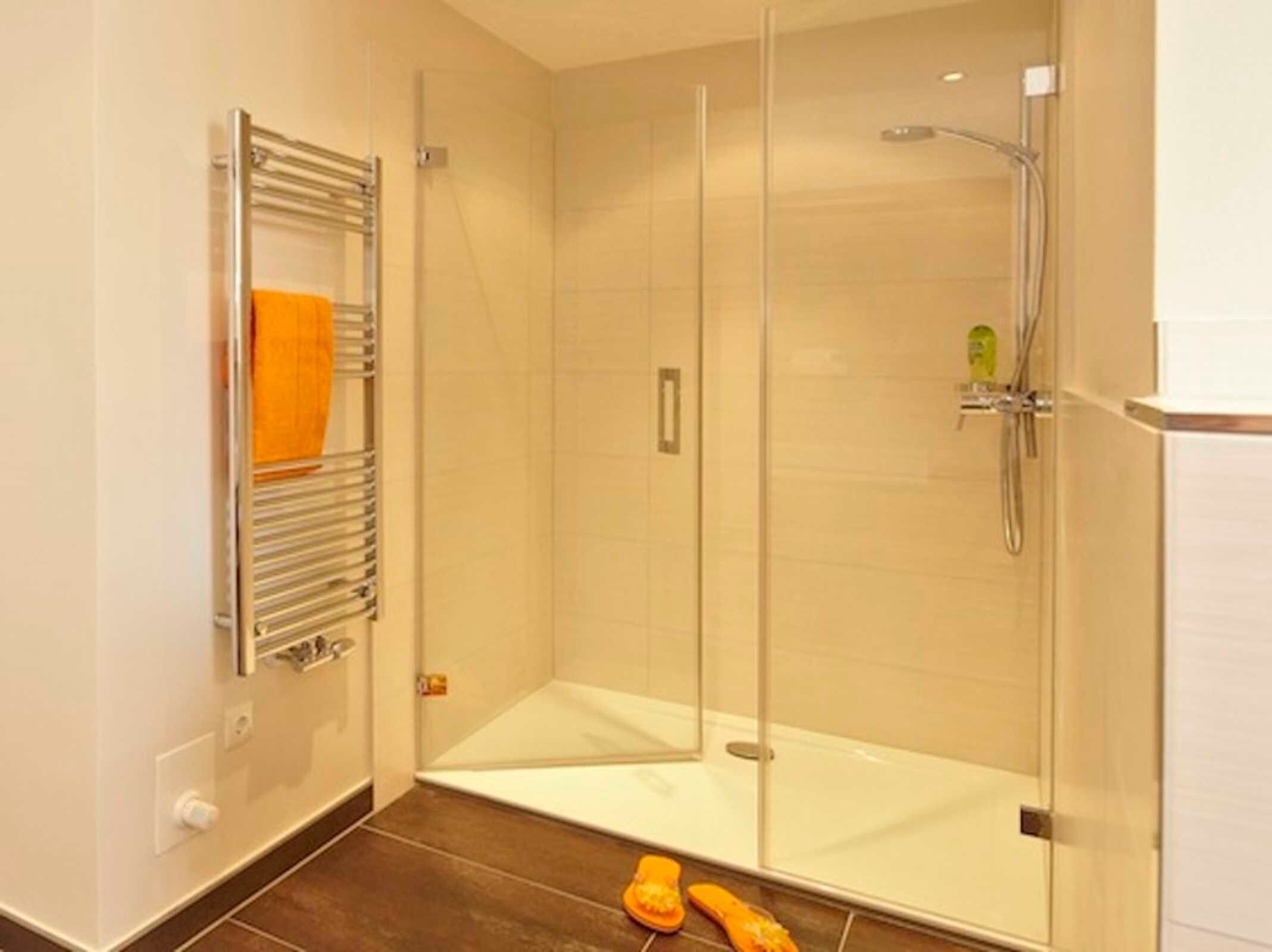 Un baño moderno con cabina de ducha de vidrio, un perchero y un dispensador de jabón visible.