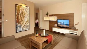 A modern living room with a wooden coffee table, beige sofas, a flat-screen TV, and a large abstract painting. - App. 4 / Nr. 4 - Dune House Aurell - directly on the Baltic Sea beach (Heringsdorf)