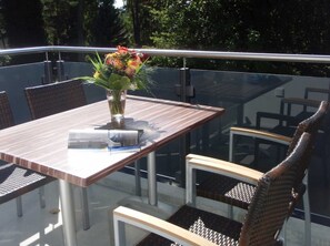 Et spiseområde med et glasbord, fletstole og en vase med blomster.
