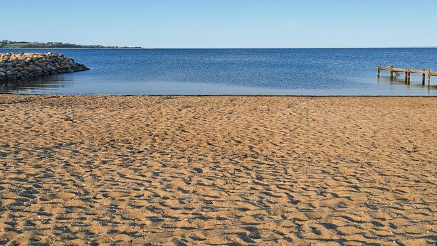 A sandy beach with a calm sea, a rocky breakwater, and a wooden pier. - Awesome home in Aabenraa with sauna (Aabenraa)