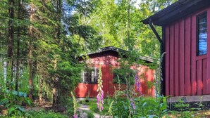 Una cabaña de madera roja rodeada de vegetación densa y un camino de grava.