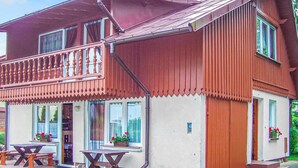 Uma casa de madeira de dois andares, com varanda, janelas e um pequeno espaço de estar ao ar livre.