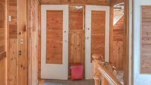 Corredor interno de madeira com duas portas, uma lixeira vermelha e um tapete azul no chão.