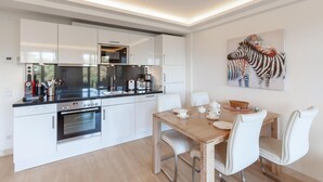 A modern kitchen with white cabinetry, a built-in oven, and a dining area with a wooden table and white chairs. - 1 bedroom lovely apartment in Binz (Prora/Rügen)