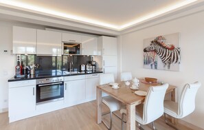 A modern kitchen with white cabinetry, a built-in oven, and a dining area with a wooden table and white chairs. - 1 bedroom lovely apartment in Binz (Prora/Rügen)