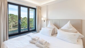 A hotel room with a large bed, white linens, and a view of trees through floor-to-ceiling windows. - 1 bedroom lovely apartment in Binz (Prora/Rügen)