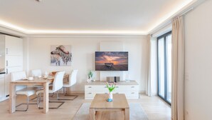 A modern living room with a wooden coffee table, white sofa, and a flat-screen TV mounted on the wall. - 1 bedroom lovely apartment in Binz (Prora/Rügen)