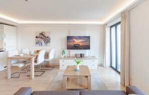 A modern living room with a wooden coffee table, white sofa, and a flat-screen TV mounted on the wall. - 1 bedroom lovely apartment in Binz (Prora/Rügen)