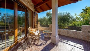 A covered patio with wicker furniture, stone walls, and a view of trees. - Cozy home in Zgaljici with sauna (Zgaljici)