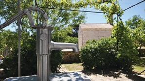 An outdoor water fountain with a stone wall and greenery in the background.