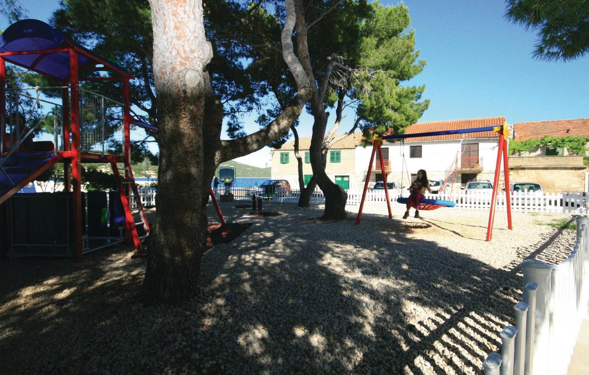 A playground with swings and climbing structures, surrounded by trees and a white fence.