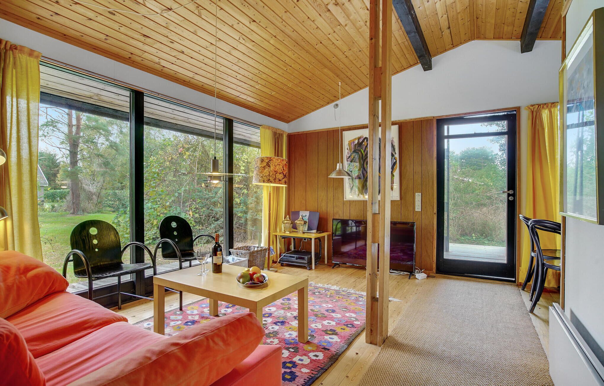 Un salon moderne avec un plafond en bois, de grandes fenêtres, un canapé, une table agrémentée d’objets décoratifs et un téléviseur.
