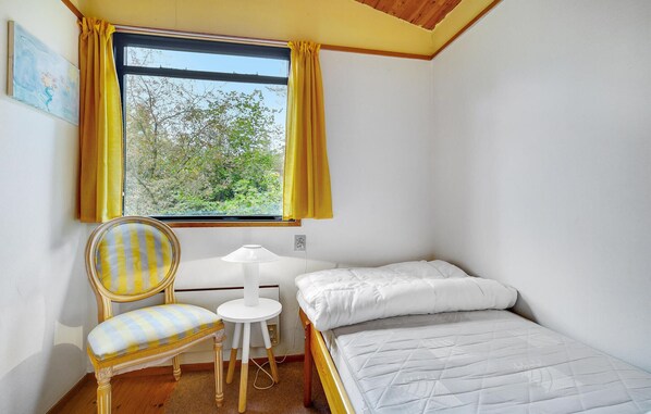 A small, tidy room with a bed, a chair, a table, and a window with curtains. - 3 bedroom beautiful home in Idestrup (Idestrup)