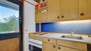 A compact kitchen with wooden cabinets, a stove, and a sink. - 3 bedroom beautiful home in Idestrup (Idestrup)